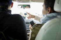 Young couple in car while woman holding smartphone and pointing directions — Stock Photo