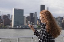 Jeune femme d'affaires au bord de l'eau avec smartphone, New York, USA — Photo de stock