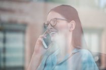 Window view of young female office worker making smartphone call — Stock Photo