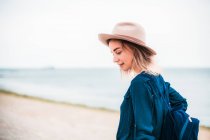 Femme en chapeau marchant le long de la plage — Photo de stock