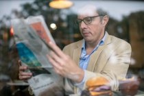 Hombre en la cafetería leyendo el periódico - foto de stock