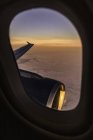 Pôr do sol paisagem nublada e asa do avião através da janela do avião — Fotografia de Stock