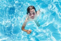 Ritratto sopraelevato del ragazzo che calpesta l'acqua nella piscina all'aperto illuminata dal sole — Foto stock