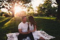 Романтична молода пара сидить в парку тримаючи руки на заході сонця — стокове фото
