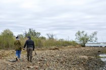 Vista trasera de una joven pareja de pescadores paseando por la playa de guijarros - foto de stock