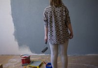 Rückansicht einer jungen Frau, die zu Hause auf eine grau gestrichene Wand blickt — Stockfoto