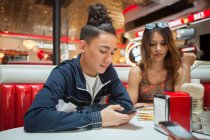 Jeune couple, assis dans le restaurant, jeune homme regardant smartphone, femme avec une expression ennuyeuse — Photo de stock