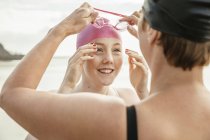 Mother and daughter adjusting swimming goggles on beach — Stock Photo
