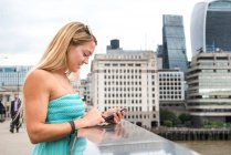 Mujer de pie en el Puente de Londres y usando smartphone - foto de stock