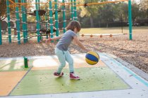 Маленькая девочка прыгает мяч на детской площадке в дневное время — стоковое фото