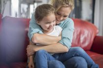 Mother and daughter on sofa cuddling and smiling — Stock Photo