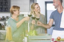 Три друга на кухне держат бокалы для вина — стоковое фото