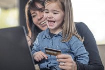 Chica y madre usando el ordenador portátil y la tarjeta de crédito para compras en línea - foto de stock
