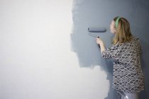 Jovem no degrau escada aplicando tinta cinza na parede em casa — Fotografia de Stock
