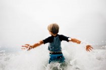 Молодий хлопчик, що йде у хвилі, вид ззаду — стокове фото