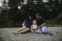 Pregnant couple sitting on beach with male toddler son, Lake Ontario, Canada — Stock Photo