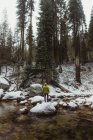 Rear view of male hiker looking at snowy forest from river, Yosemite Village, California, USA — Stock Photo