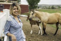 Porträt einer jungen Frau auf einem Bauernhof, Pferd und Fohlen im Hintergrund — Stockfoto