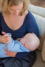 Женщина кормит грудью маленького сына на диване — стоковое фото