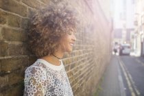 Side portrait of Young smiling woman leaning back against wall — Stock Photo