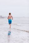 Boy running along water's edge at beach, rear view,  Dauphin Island, Alabama, USA — Stock Photo