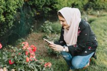 Молода жінка в хіджабі робить фото квітів на смартфоні — стокове фото