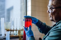 Técnico de laboratorio examinando vaso de precipitados de biocombustible rojo en laboratorio de plantas de biocombustible - foto de stock