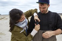 Young fishing couple fastening waders on beach — Stock Photo