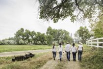 Vue arrière de couples d'âge mûr se promenant avec de jeunes femmes le long de la piste de terre de ranch, Bridger, Montana, États-Unis — Photo de stock