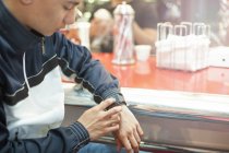 Vista de corte meados de jovem usando smartwatch sentado na lanchonete — Fotografia de Stock