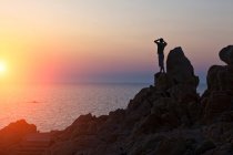 Silhouette d'homme sur des rochers regardant le coucher du soleil sur la mer, Olbia, Sardaigne, Italie — Photo de stock