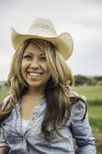 Portrait of young woman outdoors, wearing cowboy hat, smiling — Stock Photo