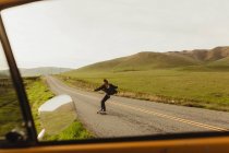 Вид на окно автомобиля молодого мужчины на скейтборде вдоль сельской дороги, Эксетер, Калифорния, США — стоковое фото