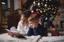 Jovem e menino lendo livro ao lado da árvore de Natal — Fotografia de Stock