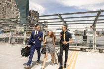 Businessmen and woman with luggage walking and talking on waterfront — Stock Photo