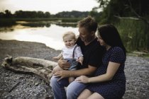 Pregnant couple sitting on beach log with male toddler son, Lake Ontario, Canada — Stock Photo