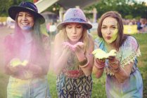 Three young women blowing colored chalk powder at festival — Stock Photo