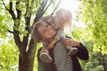 Madre dando figlia bambino sulle spalle nel parco illuminato dal sole — Foto stock