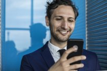 Улыбающийся молодой бизнесмен смотрит на смартфон — стоковое фото