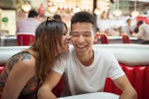 Junges Paar sitzt im Abendessen, junge Frau flüstert Mann ins Ohr und lacht — Stockfoto