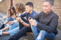 Чотири друзі сидять на вулиці, дивлячись на смартфони — стокове фото