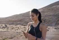 Молода жінка бігунка дивиться на смартфон в посушливому ландшафті — стокове фото