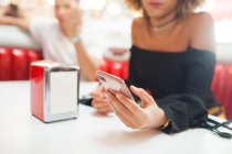 Young couple, sitting in diner, young woman using smartphone, mid section, close-up — Stock Photo
