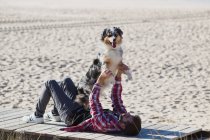 Man lying on beach boardwalk and playing with dog — Stock Photo