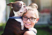 Retrato de menina carregando cão e sorrindo para a câmera — Fotografia de Stock