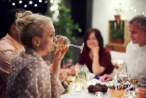 Група людей, які сидять за столом, насолоджуються їжею, молода жінка п'є з келиха вина — стокове фото