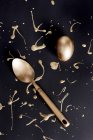 Overhead view of gold painted easter egg and spoon with splatters on black background — Stock Photo