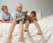 Children sitting on bed and stroking dog — Stock Photo