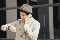 Hombre joven usando el teléfono inteligente y mirando reloj de pulsera - foto de stock