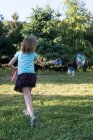 Jovem brincando com varinha de bolha no jardim, visão traseira — Fotografia de Stock